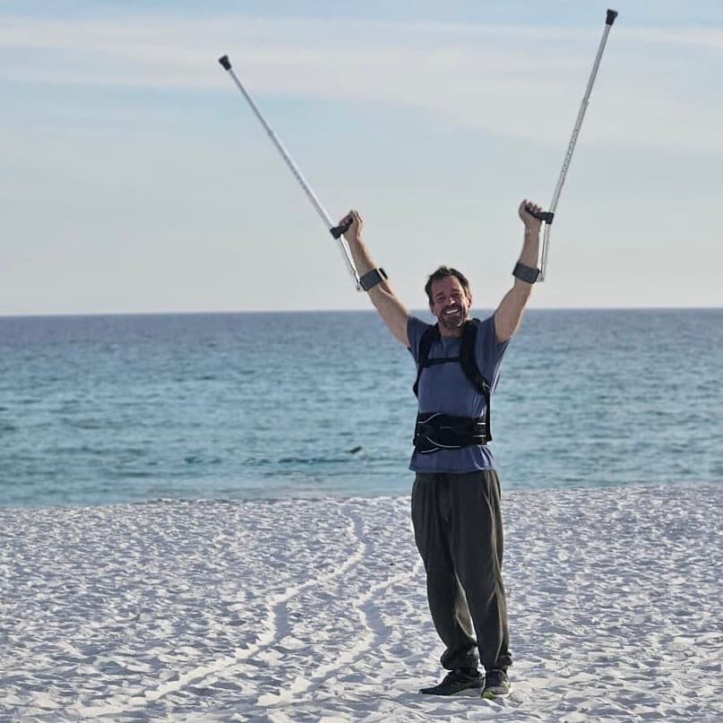 Michael Cavett with both crutches raised overhead on the beach, smiling